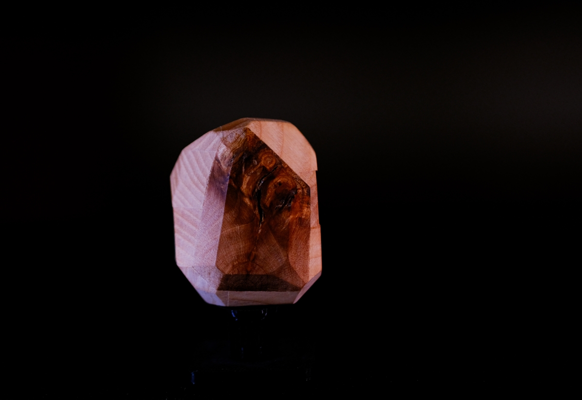 Faceted translucent gemstone with warm amber and pink hues displaying internal reflections against stark black background, creating dramatic lighting contrast