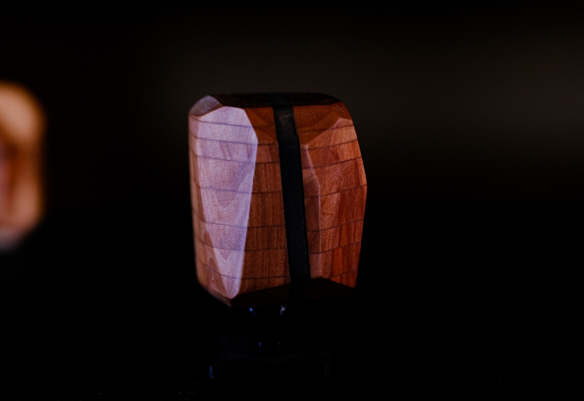 Two wooden sculptural forms with curved, segmented surfaces in warm brown and purple tones against a dark background with dramatic lighting.