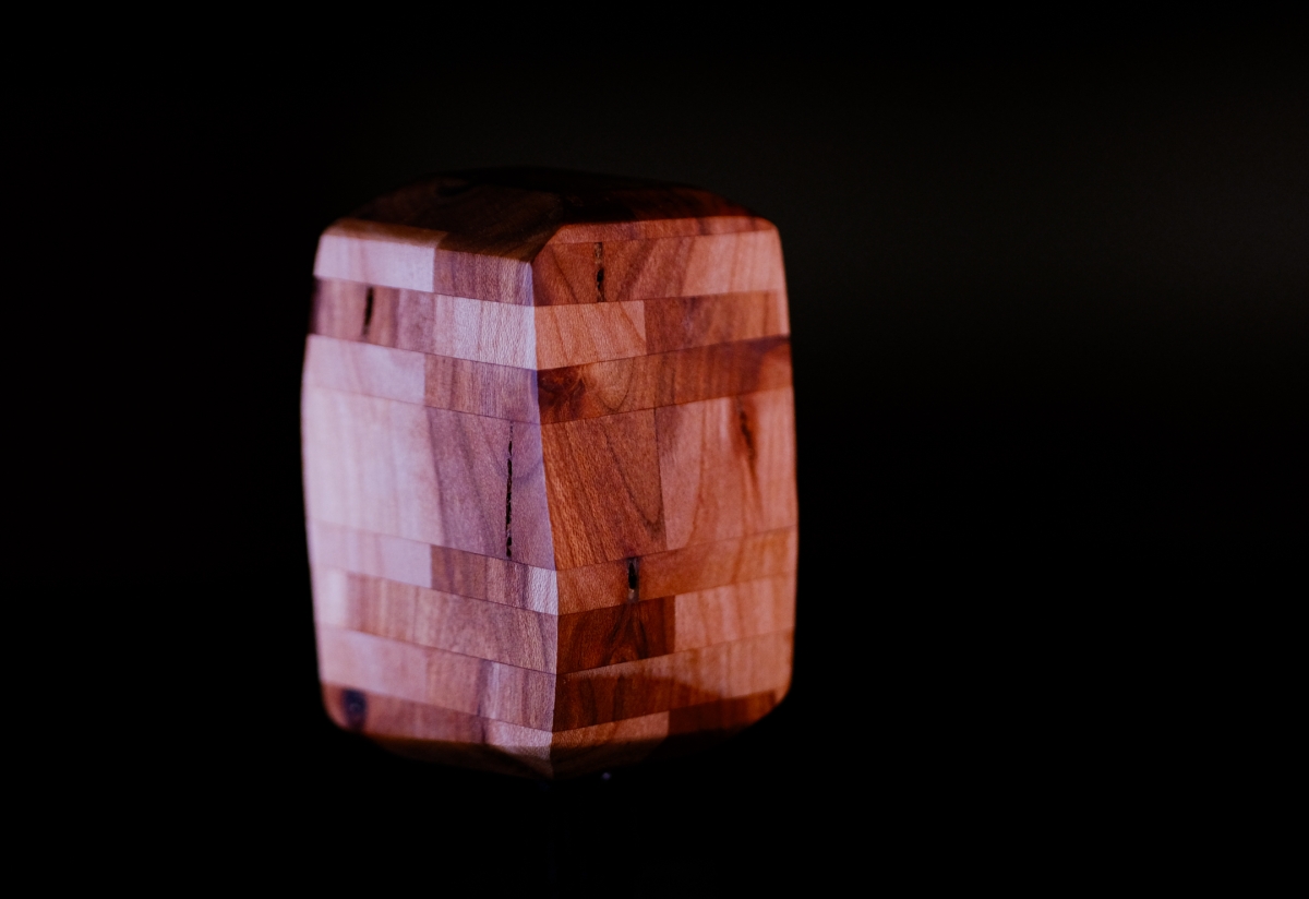 Wooden block puzzle sculpture with interlocking pieces in warm brown and reddish tones, photographed against black background with dramatic lighting