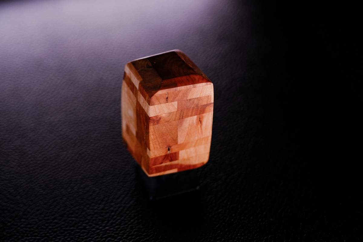 Polished reddish-brown stone cube with natural banding patterns sits on dark textured surface under dramatic purple-tinted lighting