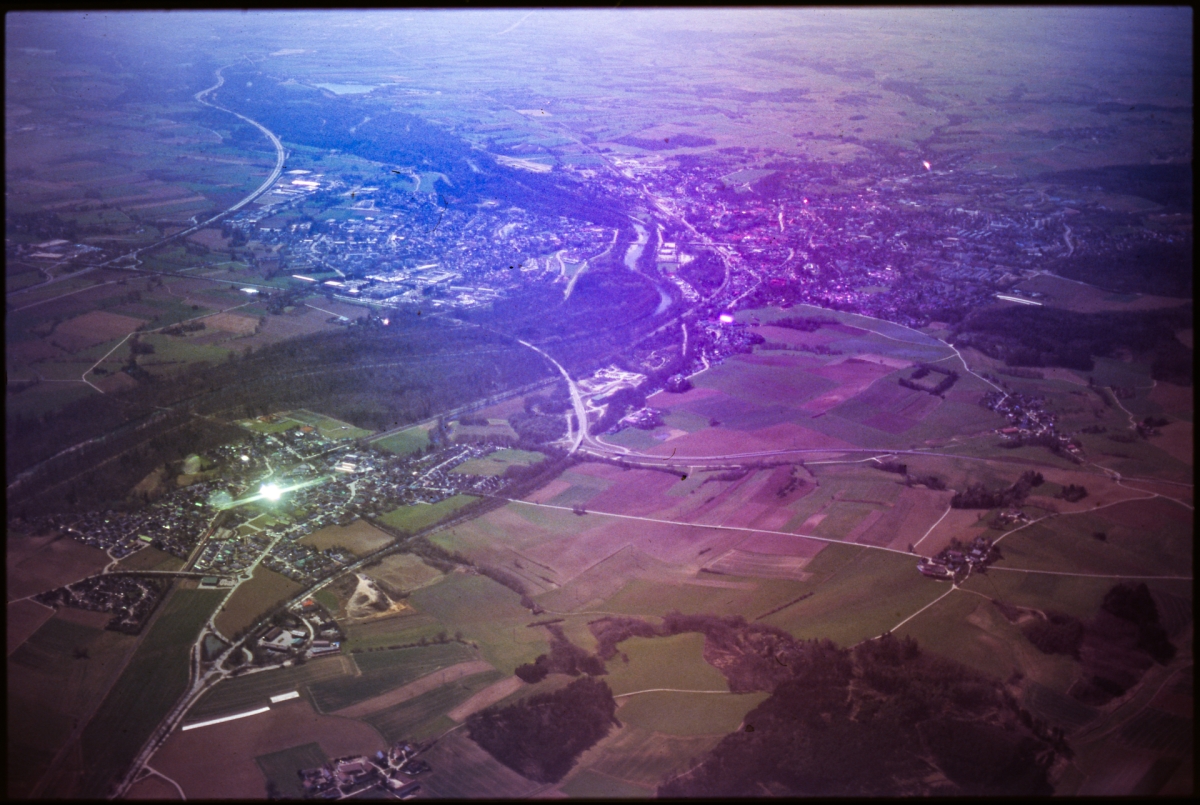 Aerial view of rural landscape with agricultural fields and small towns, bathed in dramatic purple and blue atmospheric lighting creating a dreamy, ethereal mood.