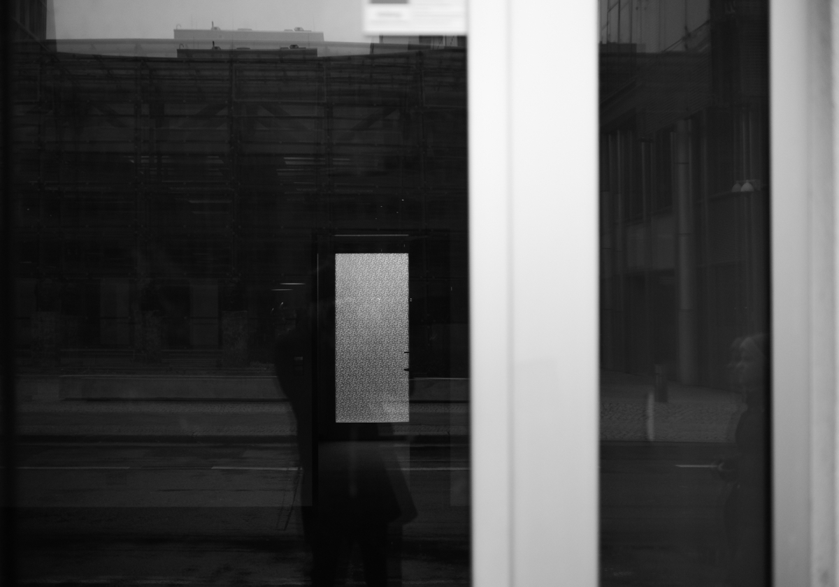 Black and white interior showing glass doors, white column, and textured rectangular panel creating geometric shadows and reflections
