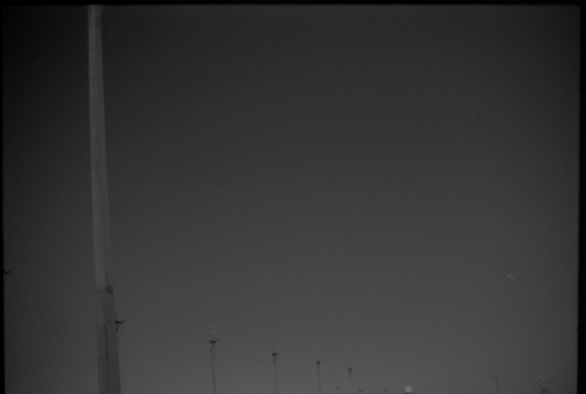 Dark, moody black and white image showing silhouettes of small figures against a stark gradient background with vertical architectural element on left side.