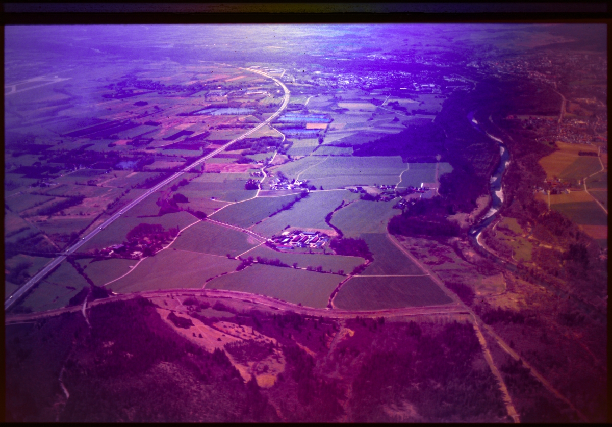 Aerial view of rural landscape with purple-tinted filter showing farmland, roads, and scattered buildings in dramatic violet hues