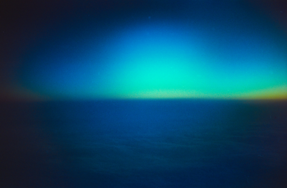 Blurred abstract composition with vibrant cyan and green light streaking across deep blue background, creating ethereal glowing horizon effect