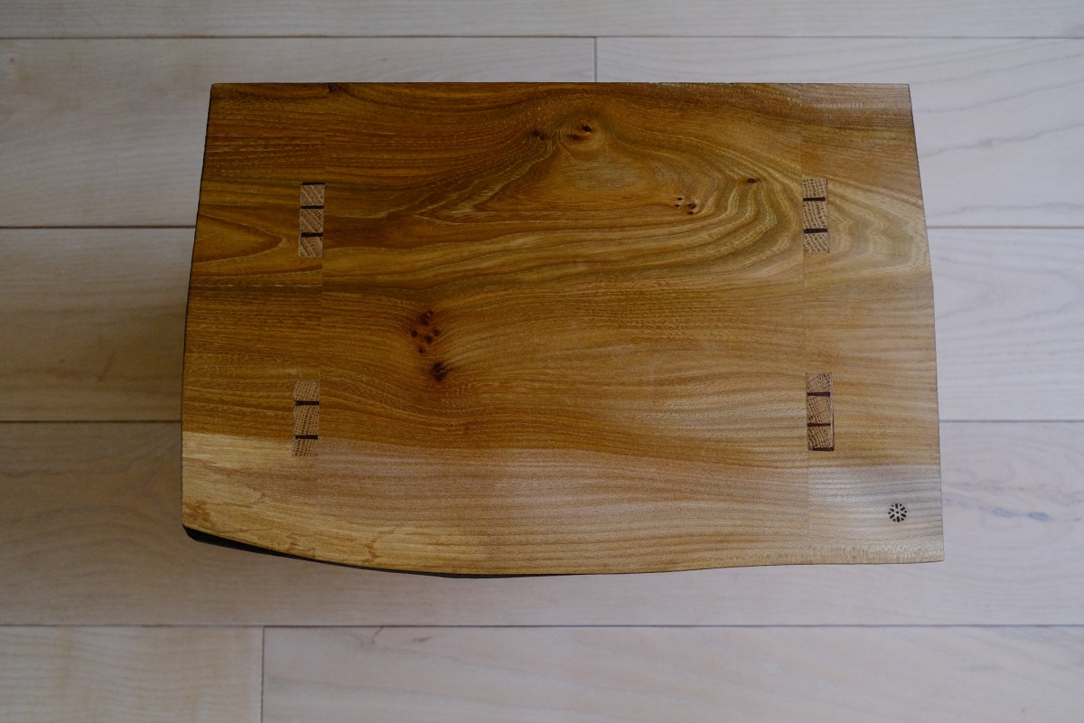 Wooden cutting board with natural grain patterns and decorative cross-hatch details, displayed on white tile flooring