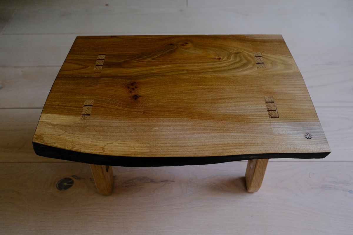 Handcrafted wooden coffee table with natural grain patterns, decorative butterfly joints, and curved edges on light wooden floor
