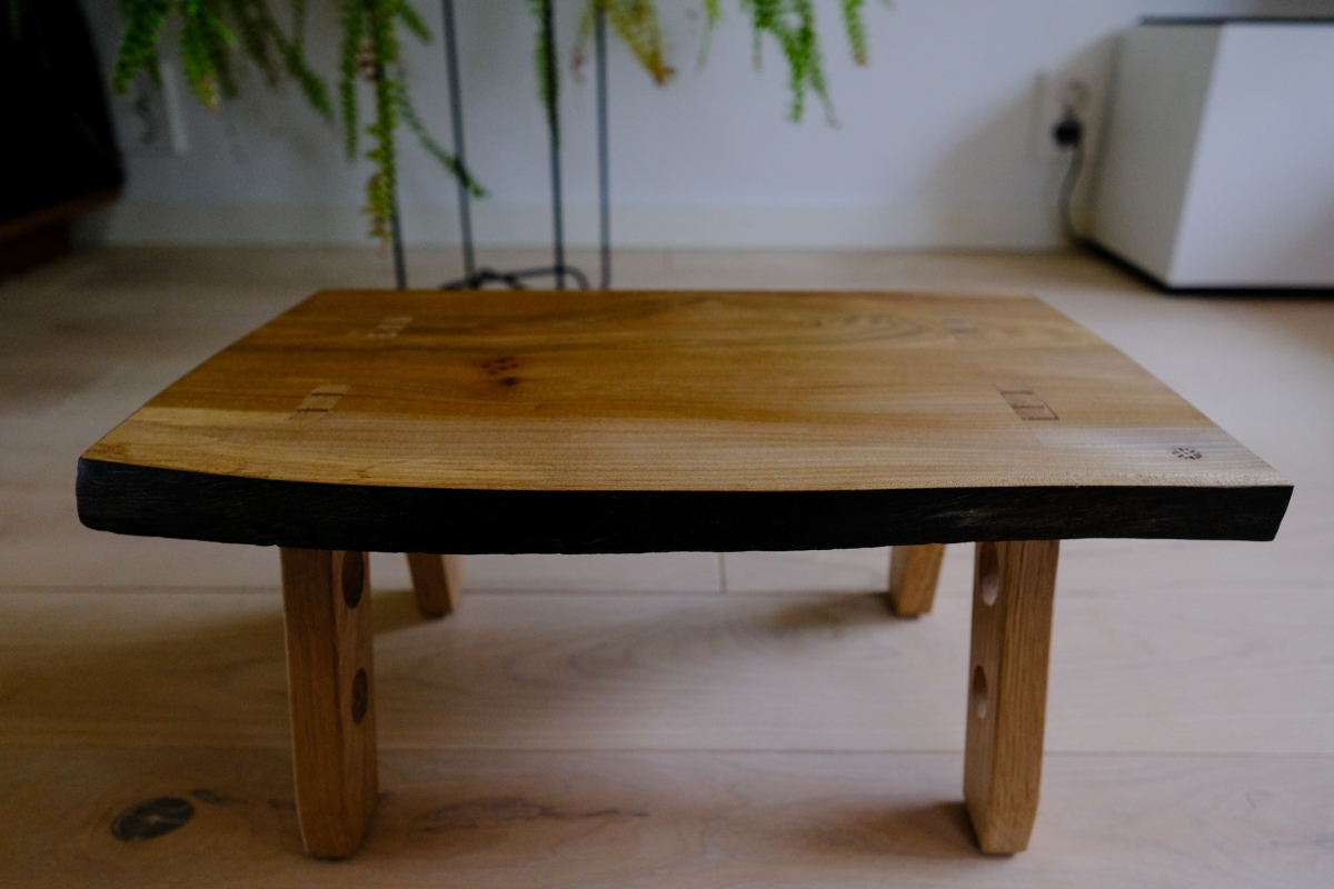 Handcrafted wooden coffee table with natural wood grain top and black painted edges, supported by curved wooden legs on light wooden floor