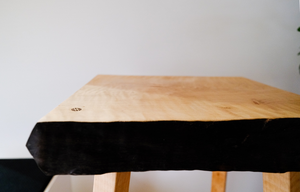 Wooden sculpture with natural wood top surface and black painted underside, supported by wooden legs against white wall background.