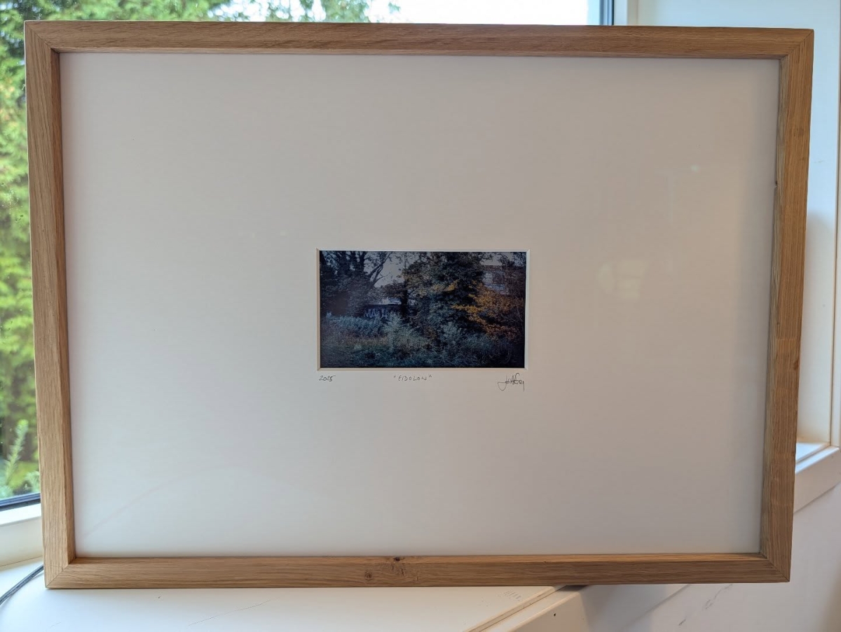 Framed abstract print titled "Obscured" showing dark moody tones of blue, brown and gray in wooden frame against white mat with window visible at edge