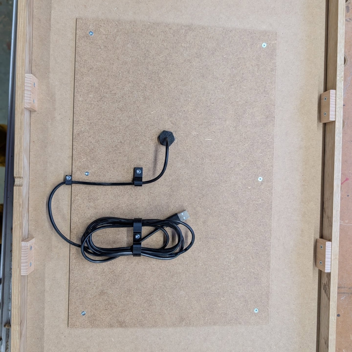 Black cable and microphone mounted on beige fiberboard with metal clips and screws, showing neat cable management installation