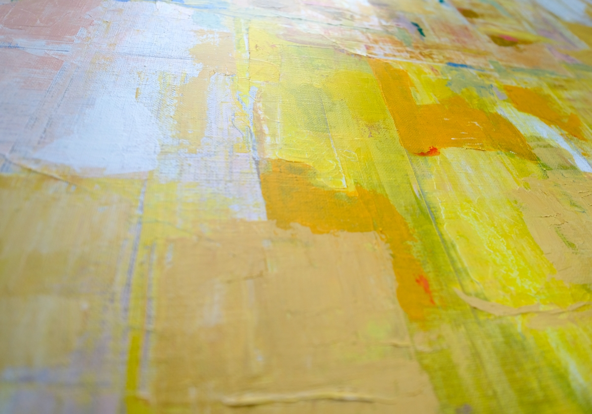Close-up of textured abstract painting with visible brushstrokes in warm yellow, orange, tan, and soft white tones on canvas.