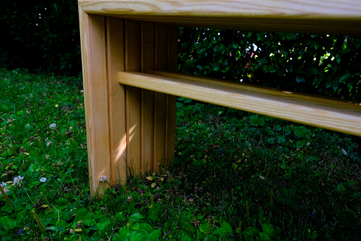 Wooden bench post and rail detail in a garden, surrounded by lush green grass, clover, and small white flowers.