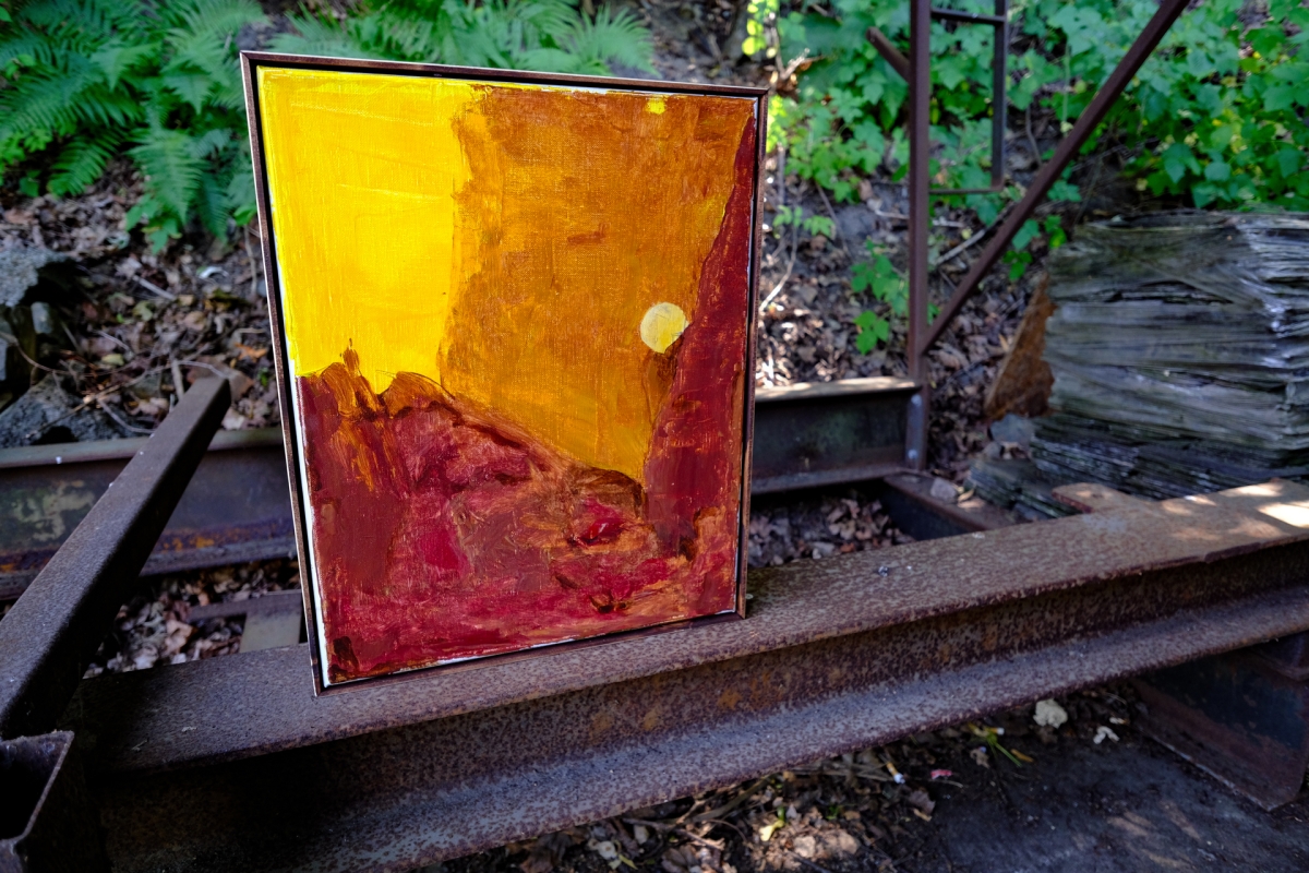Abstract painting with yellow and crimson red brushstrokes in black frame, displayed outdoors on stone steps surrounded by greenery