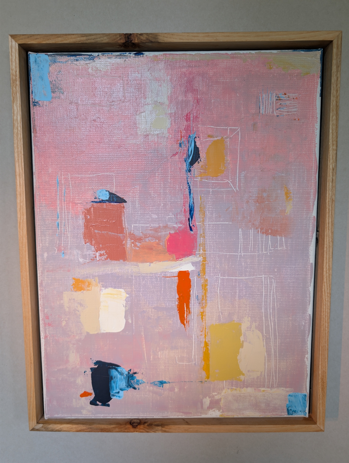 Abstract painting in a light wood frame with pink and mauve background, featuring geometric blocks of blue, orange, mustard, and navy paint.