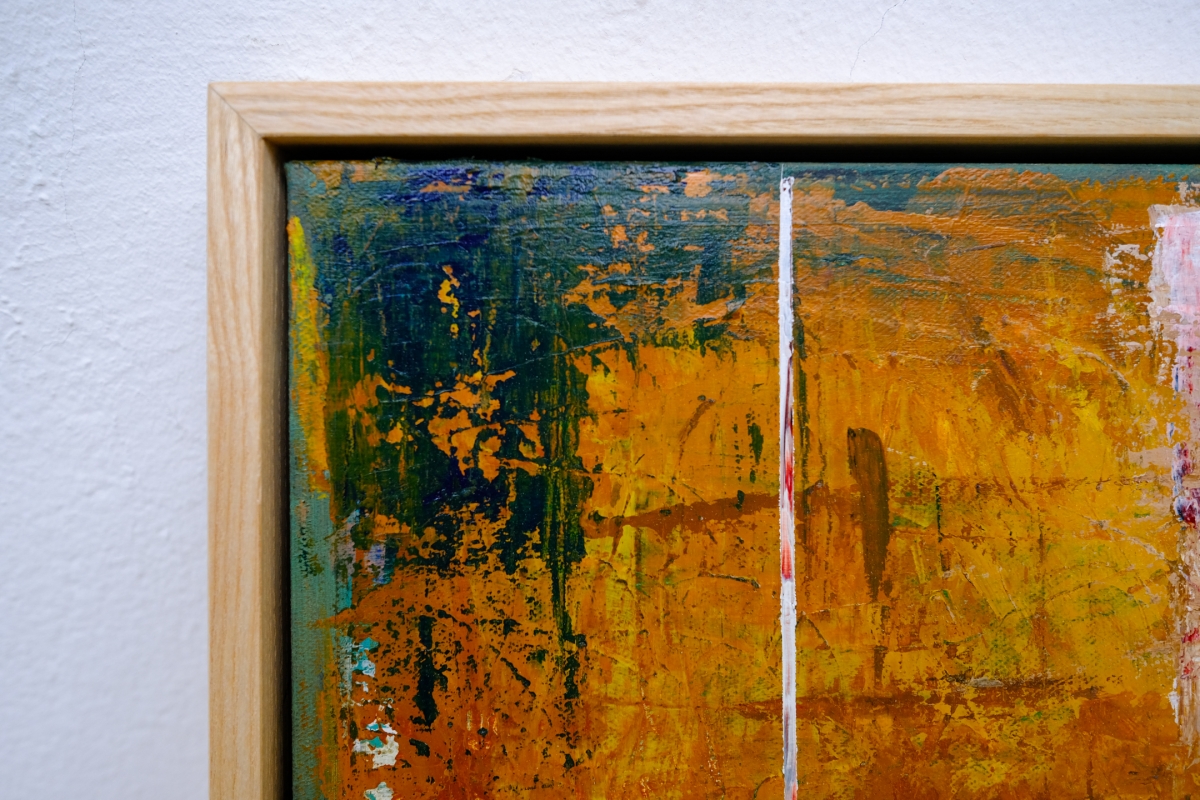Corner of an abstract painting in a light wood frame, with textured orange, blue-green, and dark teal brushstrokes and a vertical white line.