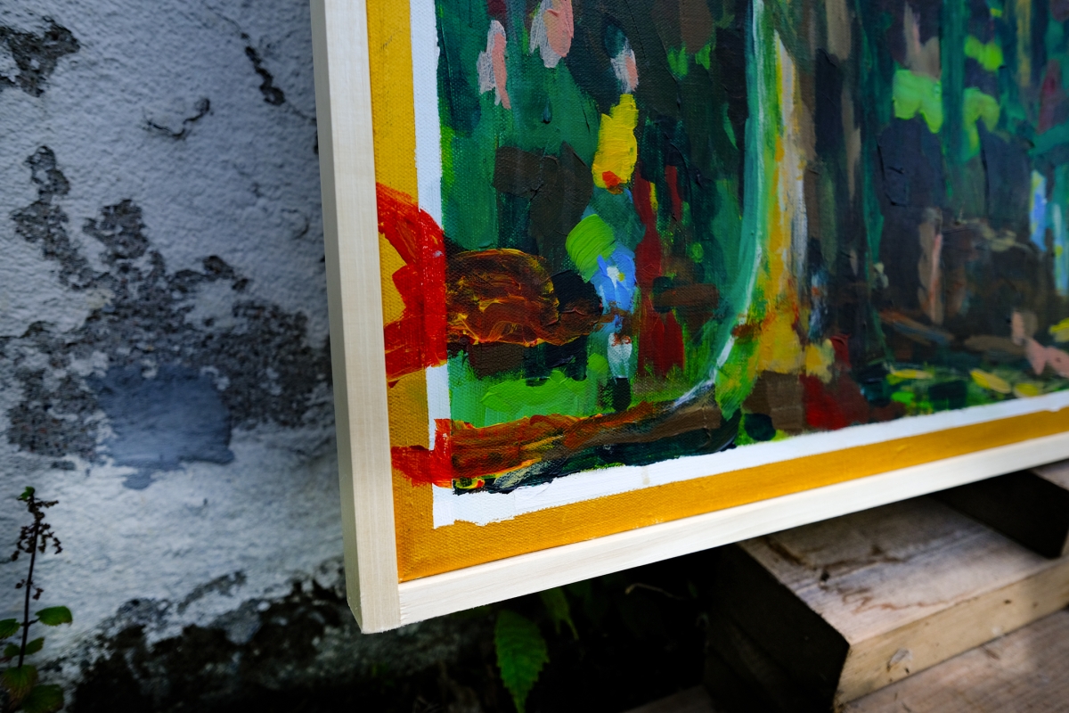 Corner of an abstract expressionist painting with bold green, red, yellow and blue brushstrokes, framed in yellow, resting against a weathered wall.