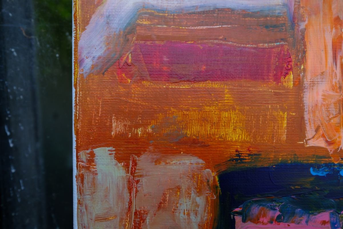 Close-up of an abstract oil painting with thick textured brushstrokes in orange, magenta, cream, and deep blue, edge of canvas visible against dark background.